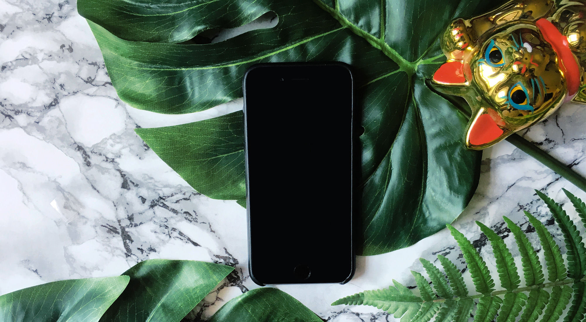Bild eines iphone und einer Winkekatze auf Marmorhintergrund mit Monstera-Pflanze